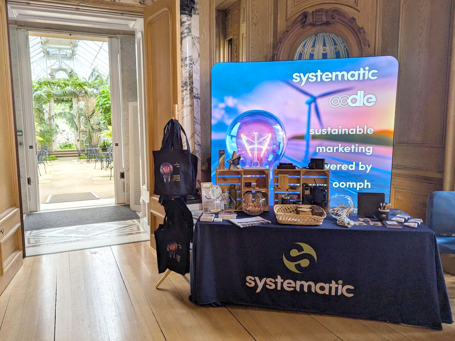 Exhibition materials for Systematic, including a branded table and a pull up lightbox behind