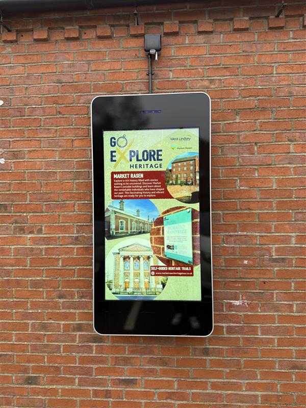 Large digital display screen featuring Go Explore travel information and photography of destinations in Lincolnshire, installed in the centre of a brick wall.
